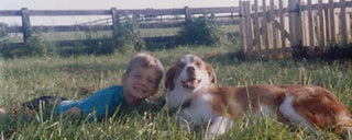 one of embark veterinary's founders, adam boyko, as a child laying in the grass with his childhood dog