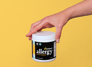 White Embark Allergy supplement tub held from above by a hand against a yellow background.