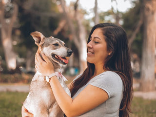 A smiling woman holding a light-brown dog outdoors.
